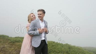 在雾的背景下，一对豪华夫妇在山上的草地上散步